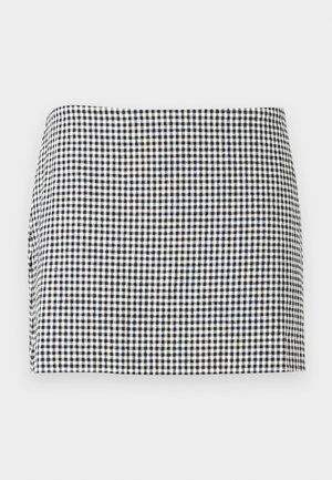 Mini-jupe à motif damier noir et blanc avec un ourlet droit sur un fond clair uni.