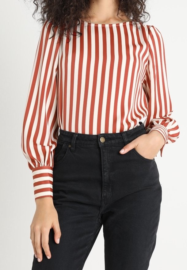 Langærmet bluse med røde og cremefarvede lodrette striber, rund halsudskæring og samlet puffærmer, parret med høj talje sorte jeans.