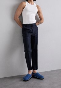 Biała prążkowana koszulka na ramiączkach, ciemnoniebieskie, dopasowane spodnie z kontrastowymi szwami oraz niebieskie wsuwane buty z brązowymi akcentami.