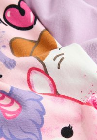 Close-up af farverige tegneserie- dyreansigter, inklusive et hvidt ansigt med brunt øre og et lilla ansigt med et lyserødt horn, på rosa stof.