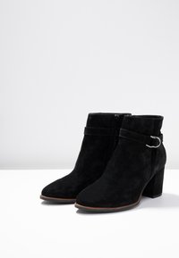 Bottines en suede noir avec un talon empilé, dotées d'une fermeture éclair sur le côté et d'une sangle décorative avec un accent en métal.