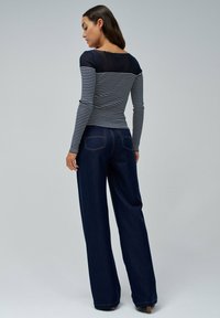 Haut rayé bleu marine et blanc à manches longues avec un col rond, associé à un jean taille large bleu foncé comportant des poches arrière et des coutures dorées.