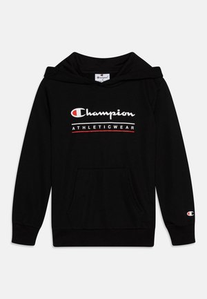 Melnas kapuces džemperis ar priekšējo kabatu, ribinātiem piedurknēm un baltiem un sarkaniem "Champion ATHLETICWEAR" logo uz krūtīm.