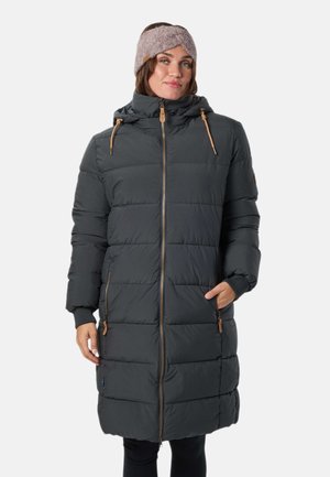 Une femme porte un long manteau matelassé gris anthracite à capuche et à cordons de serrage beige, associé à un bandeau en maille mauve, sur un fond uni.