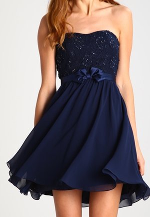 Robe cocktail bleu marine sans bretelles avec corsage brodé, ceinture en satin, détail nœud, et jupe fluide en chiffon au-dessus du genou.