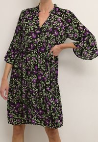 Robe fleurie noire avec des fleurs violettes et vertes, dotée de manches cloche 3/4, d'un décolleté en V et d'une jupe plissée froncée.