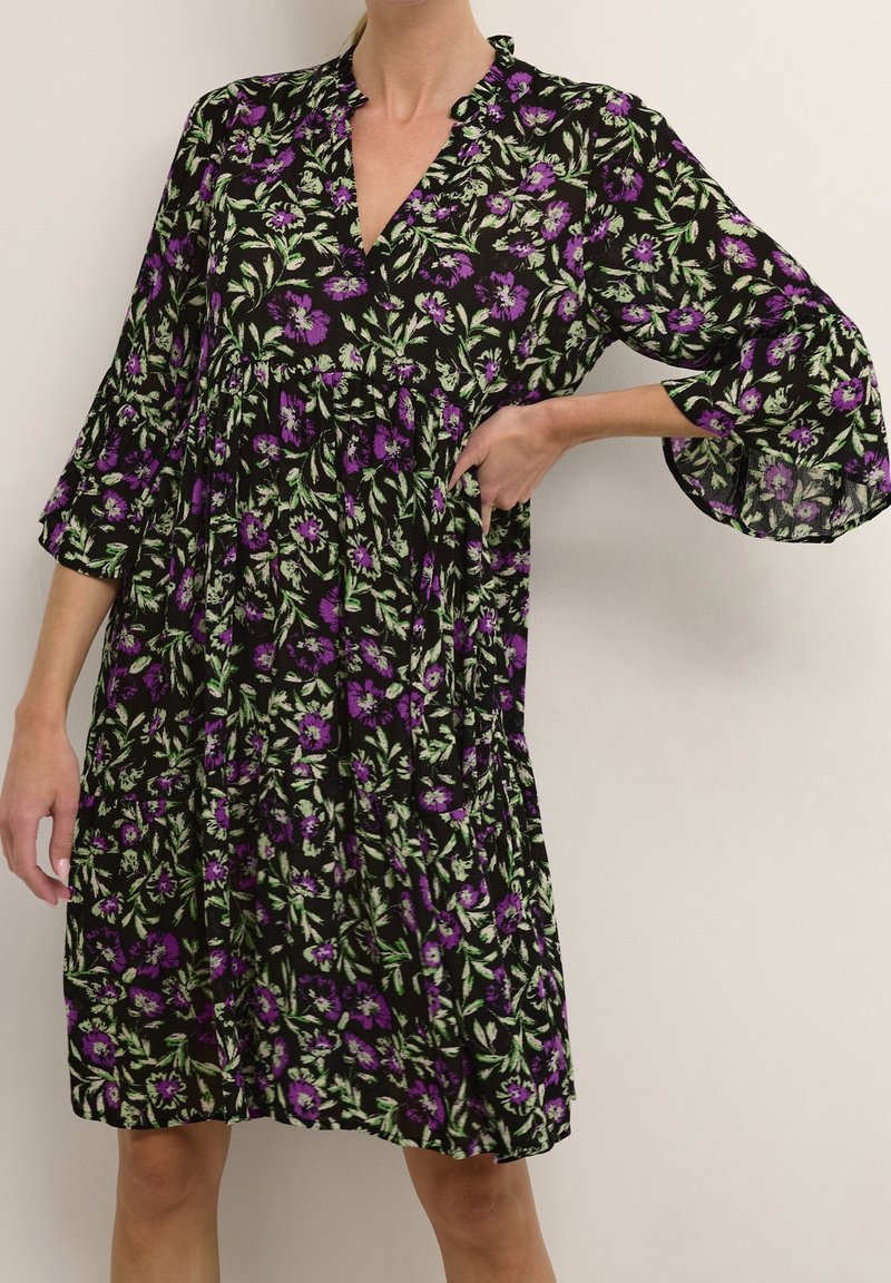 Robe fleurie noire avec des fleurs violettes et vertes, dotée de manches cloche 3/4, d'un décolleté en V et d'une jupe plissée froncée.