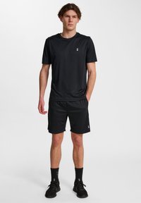 Zwart sport T-shirt en shorts van een lichtgewicht, vochtafvoerende stof. Bevat een klein wit logo op de borst en aan de zijkanten.