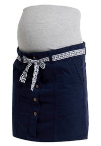 Pregnant woman wearing a grey top and navy blue buttoned skirt with patterned fabric belt tied in a bow at the waist.