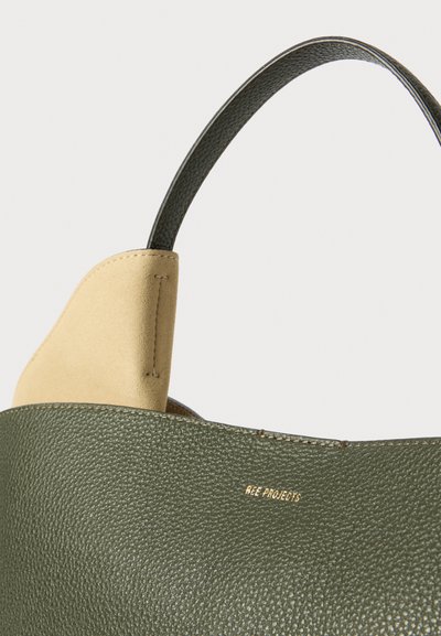 Grønt læder tote bag med et suedebånd på håndtaget. Har tekstureret overflade, kontrastfarvet detaljer og subtilt guldbelægning.