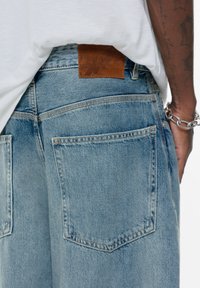 Denim kratke hlače v svetlo modri barvi, z usnjeno nalepko na pasu, dvema zadnjima žepoma in rahlo poškodovano teksturo.