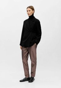 Schwarzes Blazer und schwarzer Rollkragenpullover unter einer glänzenden, metallisch braunen Hose geschichtet; schwarze Schuhe mit glatter Oberfläche. Minimalistisches Design und Texturen.