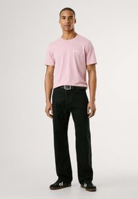 Camiseta de algodón rosa con cuello redondo, junto a unos jeans rectos negros y zapatillas negras con detalles blancos. Diseño simple, ajuste casual.