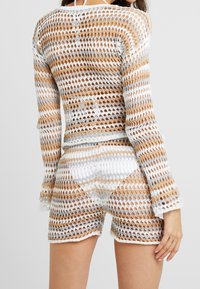 Ensemble deux pièces crocheté avec haut à manches longues et short, présentant des rayures horizontales en blanc, or et gris clair. Texture en maille ajourée.