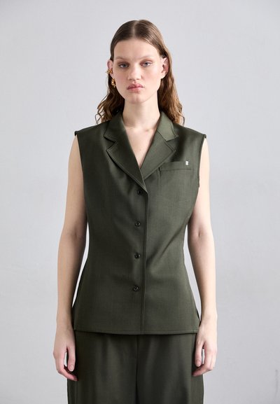 Gilet sans manches ajusté en tissu vert foncé avec une texture subtile, doté d'un revers cranté, de cinq boutons et d'une petite poche poitrine.