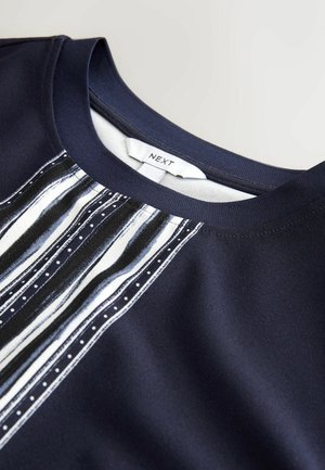 Granatowy materiałowy top z paskowanym wzorem w kolorze białym i odcieniach niebieskiego na wysokości klatki piersiowej, o gładkiej fakturze i okrągłym dekolcie. Widoczna metka.