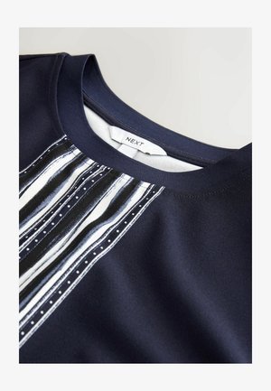 Granatowy materiałowy top z paskowanym wzorem w kolorze białym i odcieniach niebieskiego na wysokości klatki piersiowej, o gładkiej fakturze i okrągłym dekolcie. Widoczna metka.