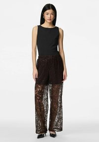 Black sleeveless top paired with dark brown lace trousers featuring a floral pattern and sequins. Glossy black heeled shoes.