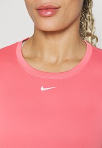Camiseta deportiva rosa con cuello redondo y mangas cortas. Presenta un pequeño logo blanco de Nike en el centro del pecho. Textura suave.