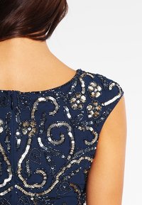 Tmavě modré šaty s propracovanou výšivkou z flitrů v metalické stříbrné a zlaté barvě, s hladkou texturou a krátkými rukávy. Zobrazen zadní pohled.