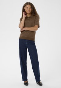 Barna, rövid ujjú pólóing, gallérral és három gombbal, sötétkék egyenes szárú farmernadrággal és fekete lapos cipővel párosítva.