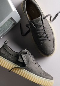Sneakers in suede grigio con una finitura testurizzata, suola in gomma e lacci coordinati. Presentano un'etichetta con marchio sul lato e un design della suola spessa.