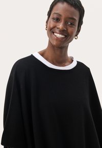 Pull noir surdimensionné avec un col rond blanc. Tissu doux, manches larges et coupe décontractée. Design minimaliste sans motifs.