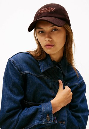 Braune Kappe mit "Tommy Jeans" in Orange gestickt, kombiniert mit einer blauen Jeansjacke mit spitzem Kragen und sichtbaren Nähten.