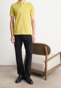 Polo à manches courtes de couleur jaune clair, en coton doux, associé à un jean noir et des chaussures en cuir noir ; design simple et classique.