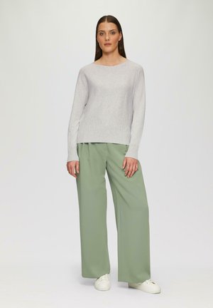 Maglione grigio chiaro a maniche lunghe con texture a coste abbinato a pantaloni verdi a vita alta e larghi. Le scarpe sono sneakers bianche.