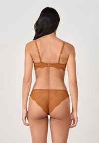 Conjunto de sujetador y bragas de encaje marrón con bordes festoneados, textura semitransparente y tirantes ajustables. El diseño incluye un patrón de puntos.
