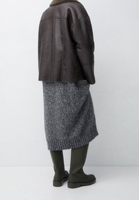 Chaqueta de cuero marrón con cuello de piel, combinada con una falda de punto gris texturizada y botas verdes hasta la rodilla. Diseño simple y moderno.