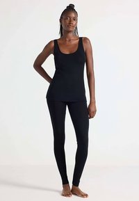 Schwarzes Tanktop mit einem runden Ausschnitt, kombiniert mit schwarzen Leggings. Der Stoff wirkt glatt, mit einer figurbetonten Passform und ohne sichtbare Muster.