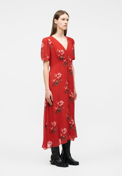 Naine punase lillelise midi-kleitidega, millel on lendlevad varrukad ja esiküljel nupud, kombineeritud mustade poolkõrgete saapadega.