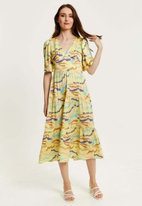 Yellow midi dress with a tiered design, featuring a colorful wavy pattern in purple, blue, and orange. Short puff sleeves and a V-neckline.