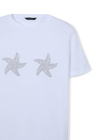 T-shirt bianco in cotone con due design di stelle marine realizzati con piccole borchie argentate sul davanti. Maniche corte e colletto tondo.