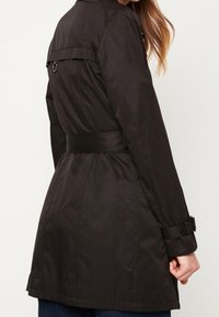 Czarny płaszcz trench z paskiem w talii, regulowanymi mankietami i subtelnymi detalami na ramionach. Gładka tekstura i wyraźna sylwetka.