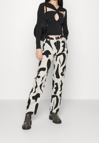 Svart långärmad topp med ett utskuret mönster, kombinerad med lösa krämfärgade byxor med djärva svarta abstrakta mönster och kraftiga svarta stövlar.