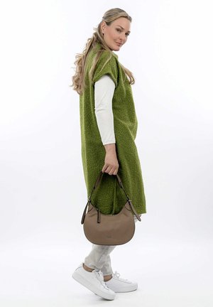 Green textured oversized sleeveless sweater dress, white long-sleeve shirt underneath, beige shoulder bag, light grey pants, white sneakers.