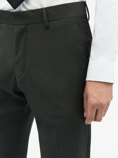 Tumed rohelised kohandatud püksid sileda tekstuuriga, millel on vöökohad, ees olevad taskud ja kitsenev lõige. Osaliselt nähtav valge särk.