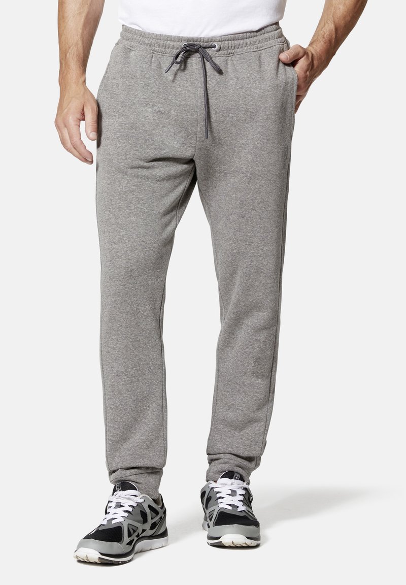 Graue Sweatpants mit einem Kordelzug-Bund, seitlichen Taschen, schmal zulaufenden Beinen und einer weichen Textur, kombiniert mit schwarz-grauen Sportschuhen.