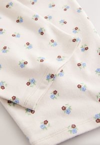 Tissu crème avec petit motif floral bleu et marron, présentant des coutures cousues et une texture douce.