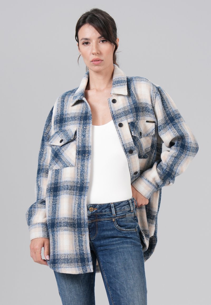Blauw en crème geruite flanellen overhemd met een knoopsluiting aan de voorkant, twee borstzakken en een losse pasvorm, gecombineerd met blauwe denim jeans.