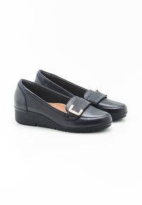Mocasines de cuero negro con un tacón bajo en forma de cuña, que presentan una banda ancha y un detalle de hebilla decorativa en la parte delantera. Textura suave, punta redondeada.