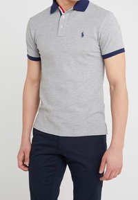 Grå pikétröja med marinblå krage och matchande ärmar, med en liten blå logotyp på bröstet. Mjuk tygkvalitet med klassisk passform.