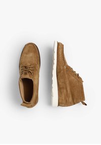 Zapatos de ante marrón con una textura suave, con suela de goma blanca, diseño de punta redonda y costuras en contraste. Cuerdas en la parte frontal.