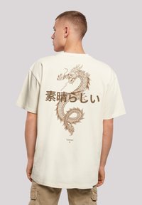 Beige cotton t-shirt featuring a large brown dragon graphic and Japanese text on the back. Short sleeves and relaxed fit.