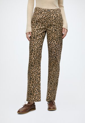 Kvinde iført leopardprint bukser med høj talje og lige ben, kombineret med brune læder snøresko og en cremefarvet ribstrikket sweater.