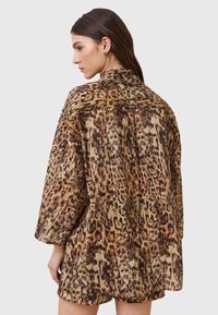 Camicia con stampa leopardata, tessuto leggero, vestibilità ampia, maniche lunghe, orlo arrotondato, dettaglio sul retro con yoke, tonalità terrose di marrone e oro.
