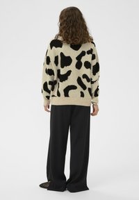 Beidzis džemperis ar lielu melnu leopardu rakstu, ribota apakšējā mala un piedurknes. Kombinēts ar brīviem melniem biksēm. Tekstūra izskatās maiga un ērta.